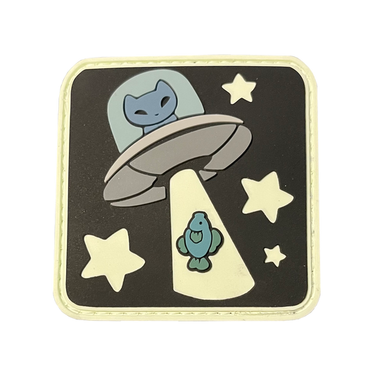 A square shaped patch featuring a blue cat inside a UFO, with a green fish going up the UFO's lightbeam. The UFO is surrounded by four stars. 